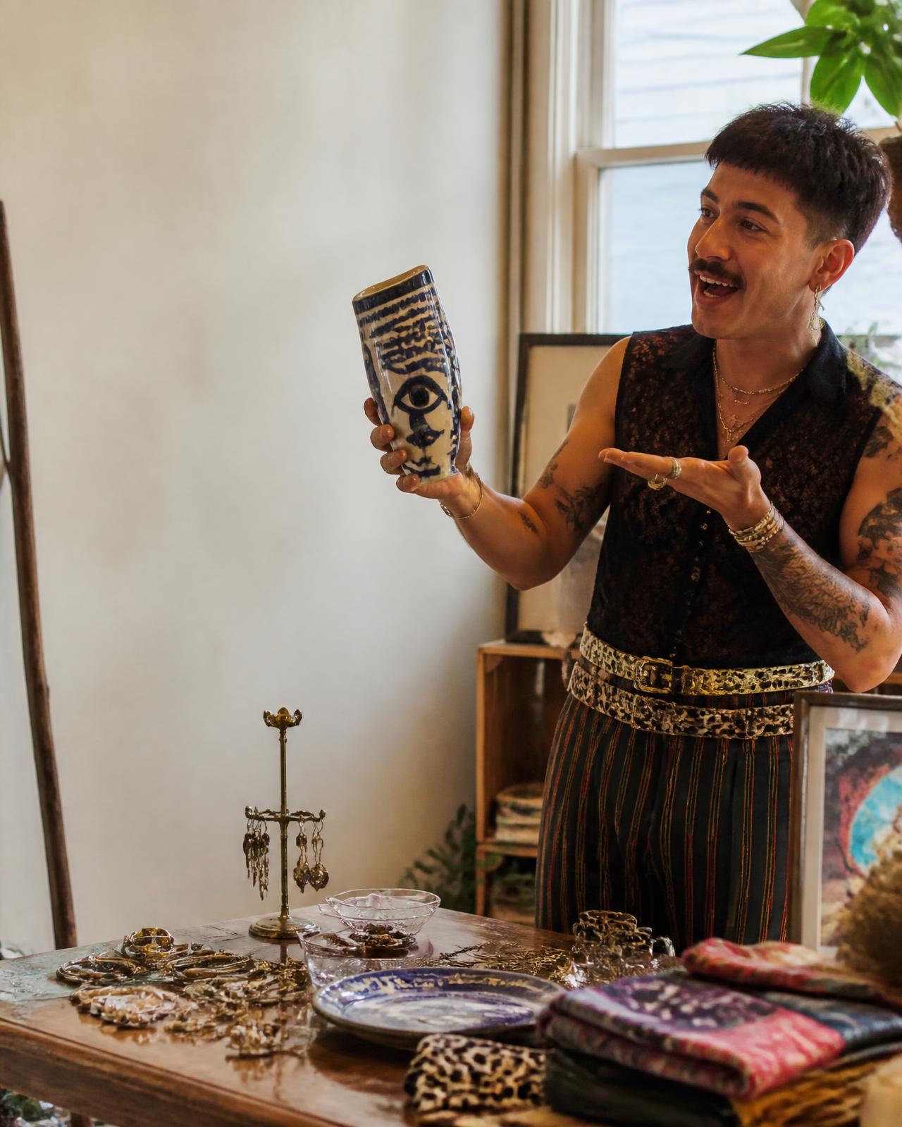 A merchant turned toward the page copy, presenting a hand-painted ceramic piece above a table of jewelry, prints and textiles